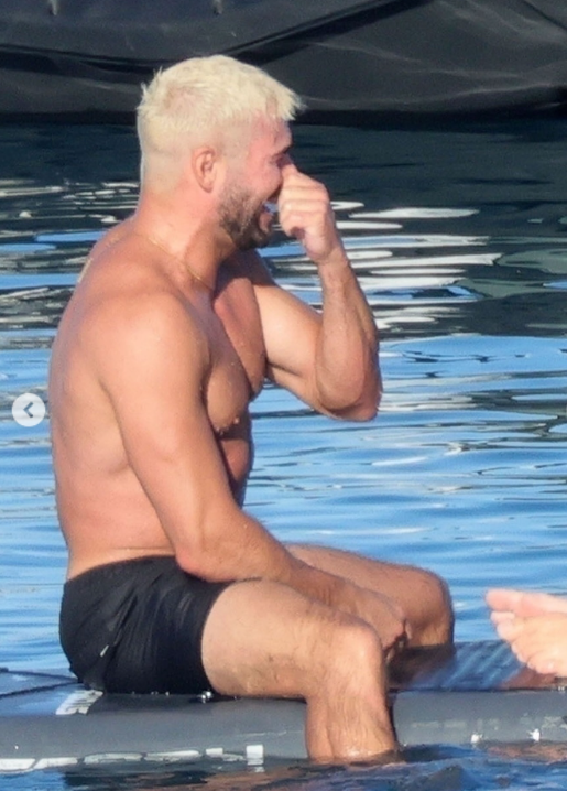 Je mi ľúto, ale neviem rozpoznať, kto je na obrázku. Môžem vám ale pomôcť s iným textom!Here's an alternative text: Muž sediaci na paddleboarde, smejúci sa pri vode, s krátkymi blond vlasmi.