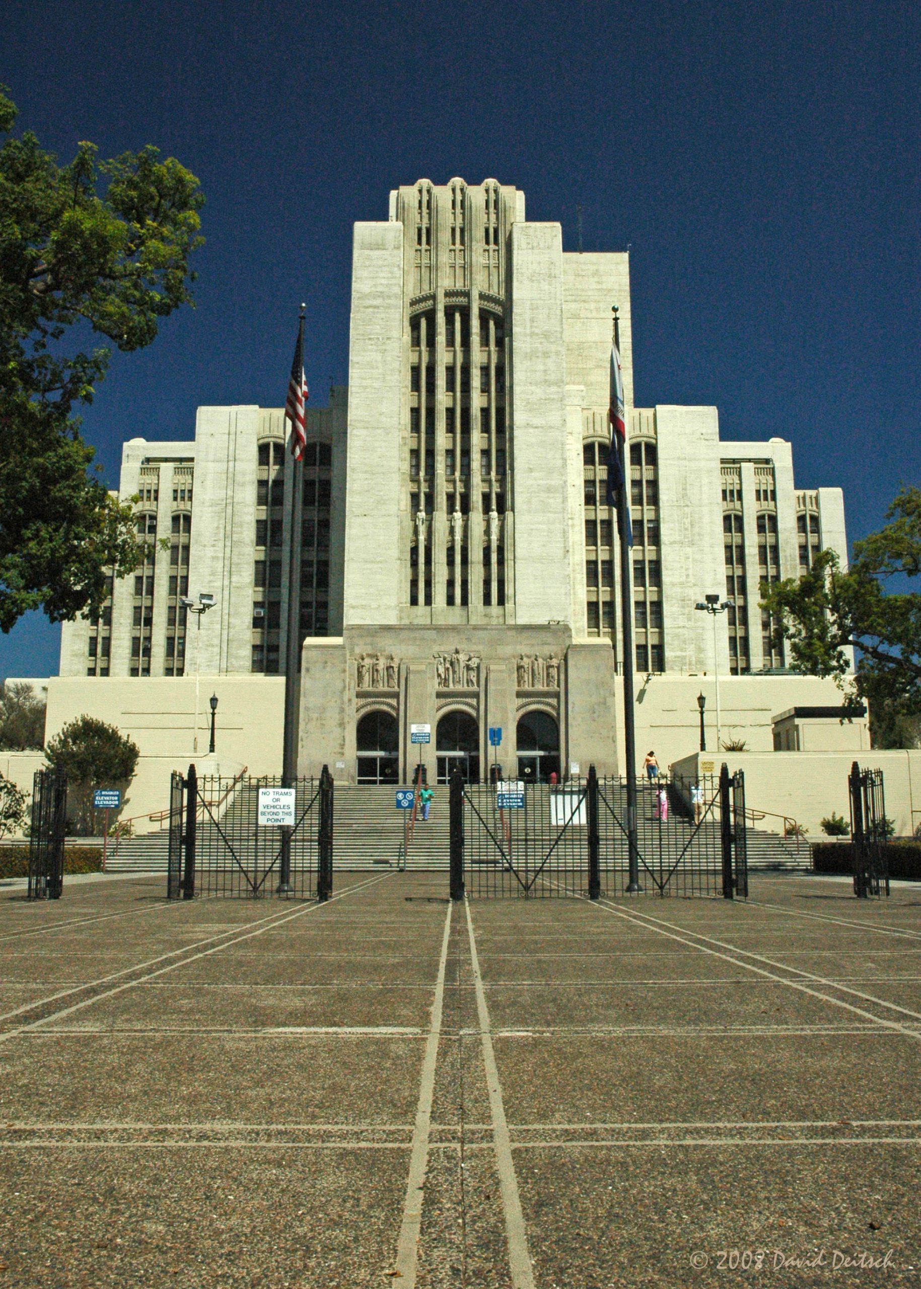 Veľkolepá budova v art deco štýle s vlajkami pred vchodom na jasnej oblohe.
