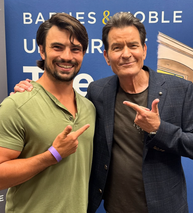 Ospravedlňujem sa, ale nedokážem identifikovať osoby na obrázku. Môžem však vytvoriť všeobecný alternatívny text:Dvaja muži pózujú pred modrým pozadím s nápisom v kníhkupectve.