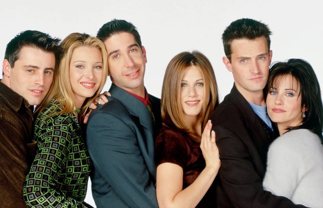 Šesť priateľov stojí blízko seba, usmievajú sa a pózujú na bielom pozadí.