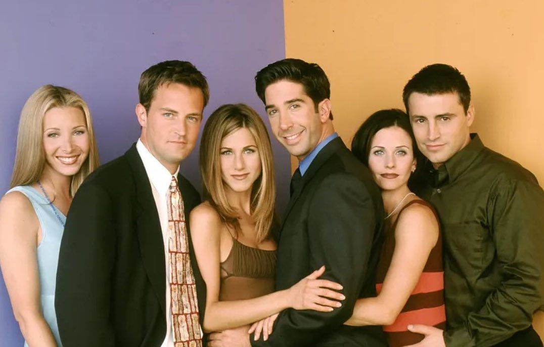 Šesť priateľov stojí vedľa seba pred farebným pozadím, všetci sú oblečení v elegantnom štýle.