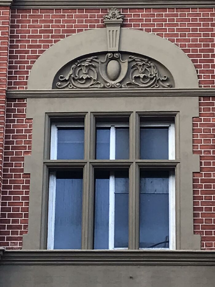 Dekoratívne okno s ornamentom na červenej tehlovej fasáde historickej budovy.