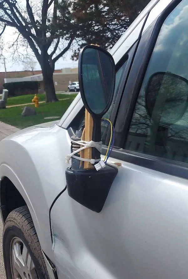 Provizórna oprava bočného spätného zrkadla auta s použitím paličky a šnúr, improvizované riešenie na opravu.