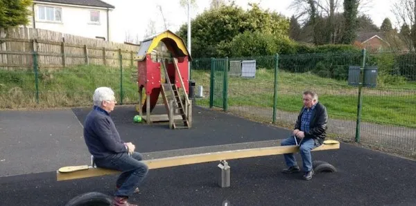 Dvaja muži na hojdačke na prázdnom ihrisku so šmykľavkou na pozadí.