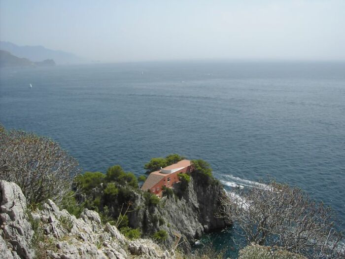 Dom na útesnej skale obklopený morom a prírodou pod modrou oblohou, idylické pobrežie na izolovanom mieste.