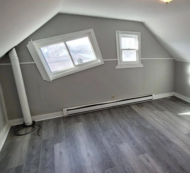 Poddrovná izba so šikmými stenami, šikmo osadeným oknom a sivou vinylovou podlahou.