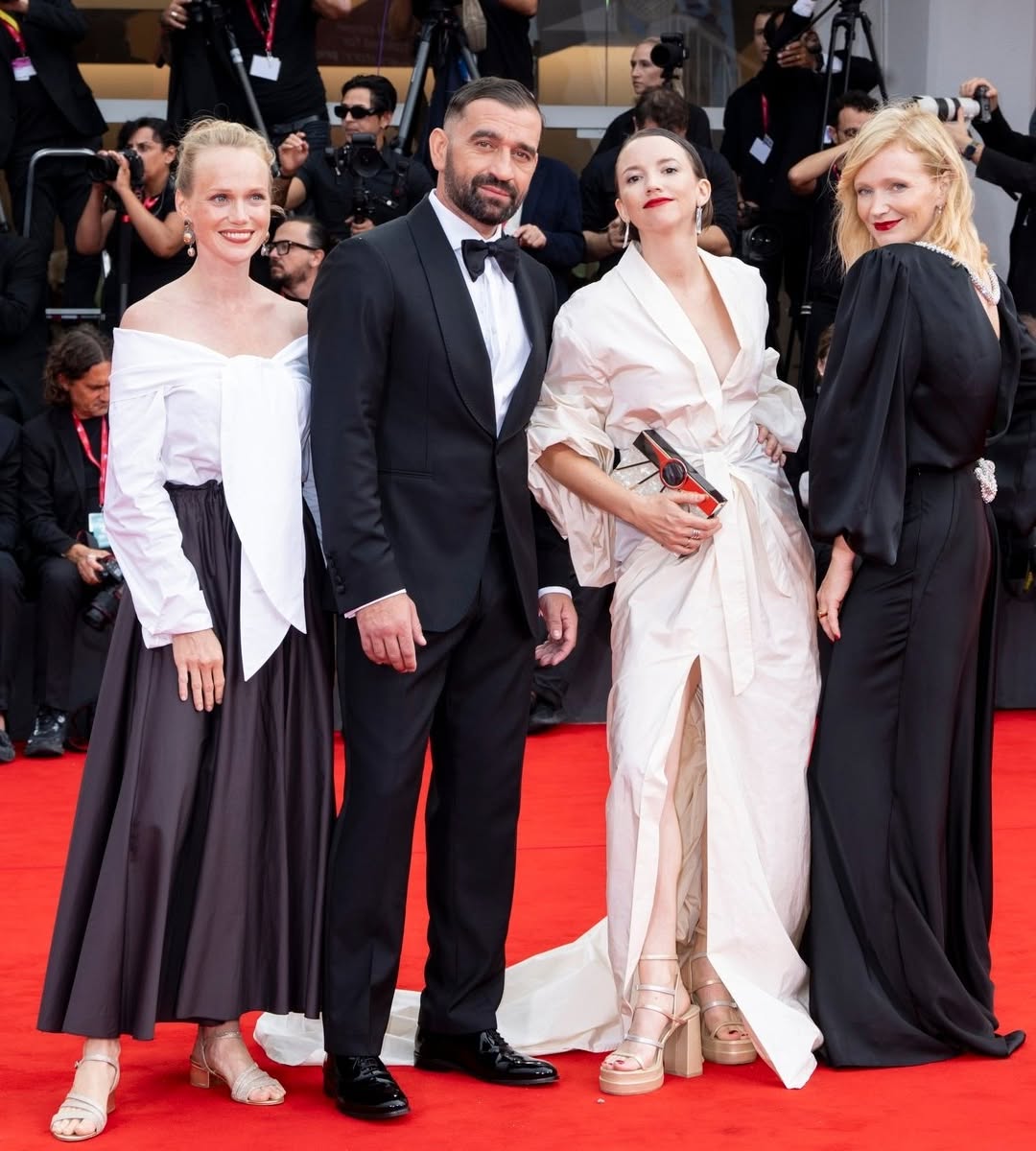 Štyri osoby na červenom koberci v elegantných outfitoch pripravené na spoločenskú akciu.