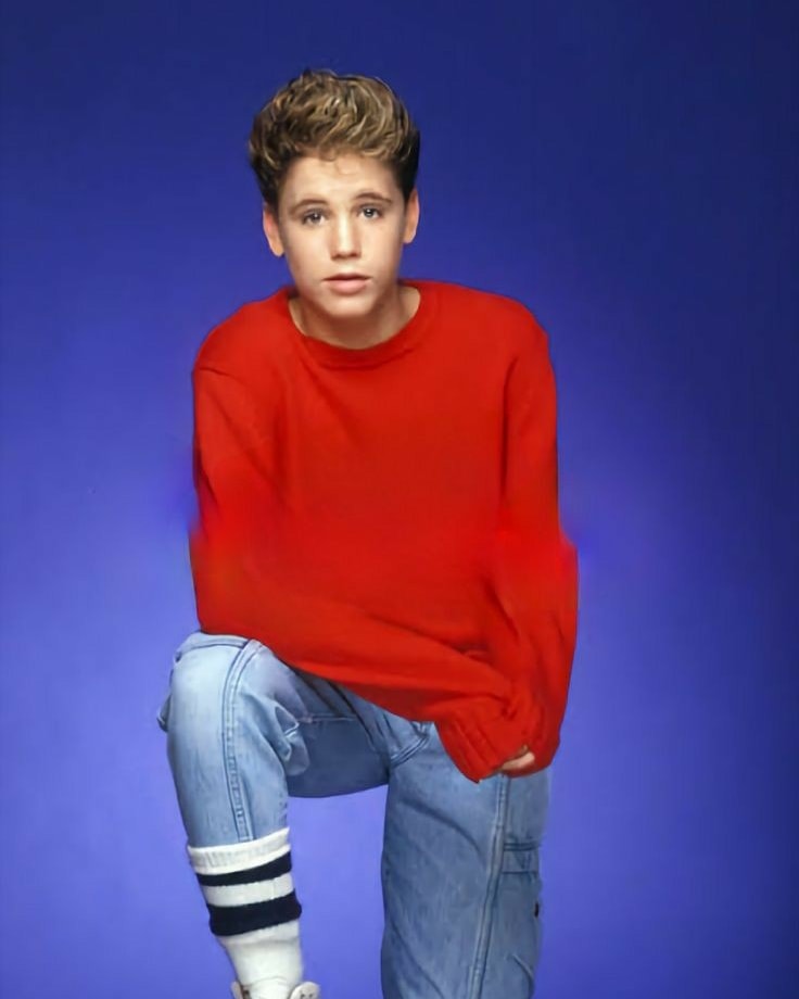 Mladý muž v červenom svetri a džínoch na modrom pozadí, módna fotografia 90. rokov.