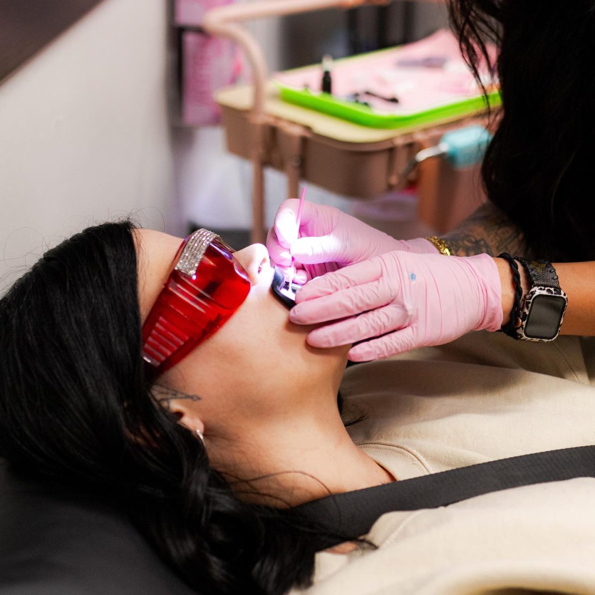 Osoba s červenými okuliarmi dostáva zubné ošetrenie, pracovník v rukaviciach používa špeciálny nástroj.