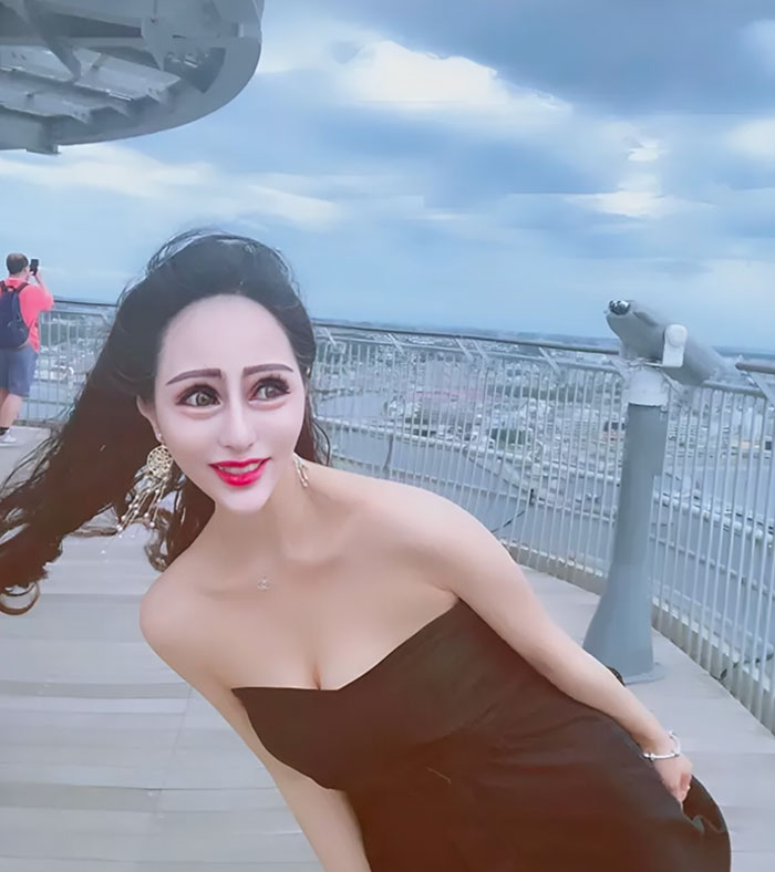 Osoba v čiernych šatách na terase s vetrom vo vlasoch, modrá obloha v pozadí.