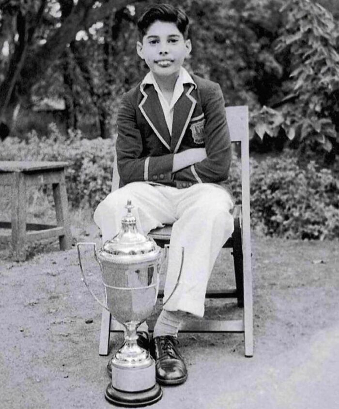 Chlapec v uniforme sedí na stoličke s veľkým trofejom, čiernobiela fotografia vonku.