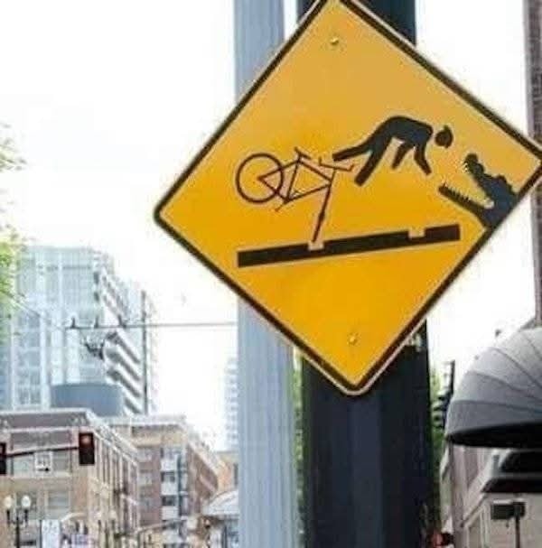 Upozornenie: Vtipná značka s piktogramom cyklistu, ktorý padá do úst krokodíla na ulici v meste.