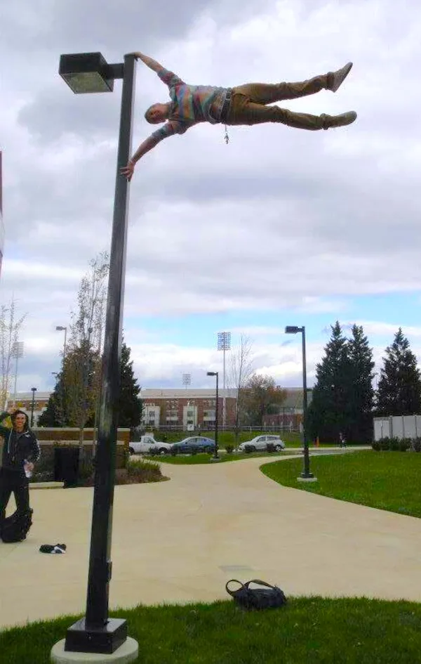 Muž vykonáva horizontálnu vlajku na stĺpe v parku pod zamračenou oblohou, ukazujúc silnú rovnováhu a odvahu.