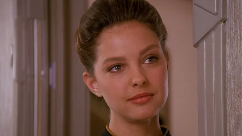 Ľutujem, neviem určiť, kto je na obrázku, ale môžem poskytnúť alternatívny text: Žena s jemným úsmevom pozerá z dverí.