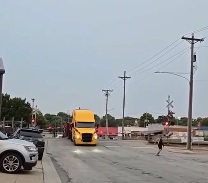 Nákladné auto prechádza cez železničné priecestie v meste, kde sú viditeľné výstražné červené svetlá.
