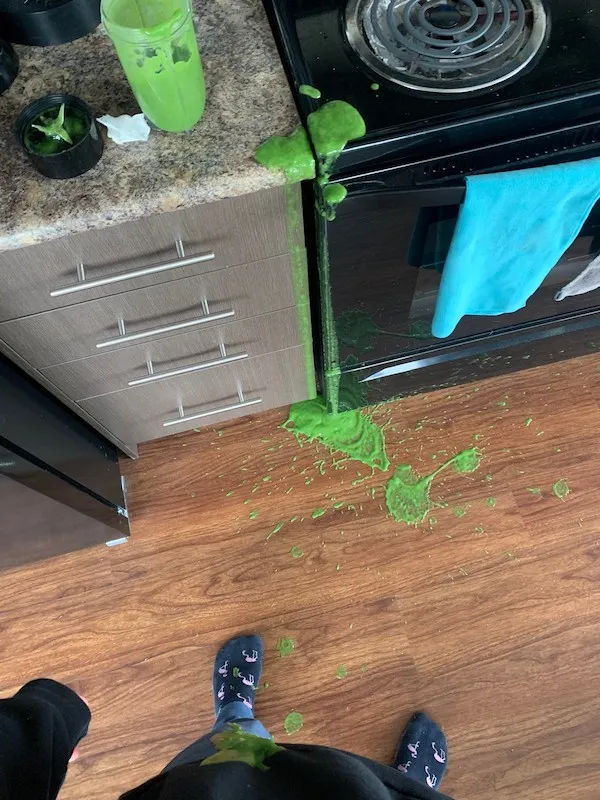 Rozliaty zelený smoothie na podlahe a linke v kuchyni vytvára chaos a neporiadok.