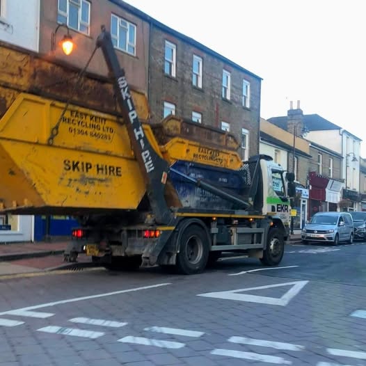 Nákladné auto prepravujúce veľký žltý kontajner na odpady na mestskej ulici.