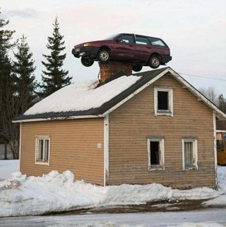 Auto na streche zasneženého domu, neobvyklá situácia v zasneženej krajine, kuriozita.