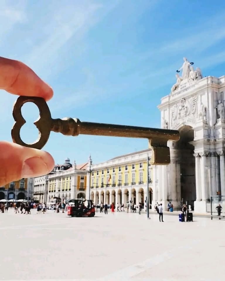 Kľúč držený pred historickou bránou v slnečnom meste, vytvárajúci optickú iluzíu zámku.