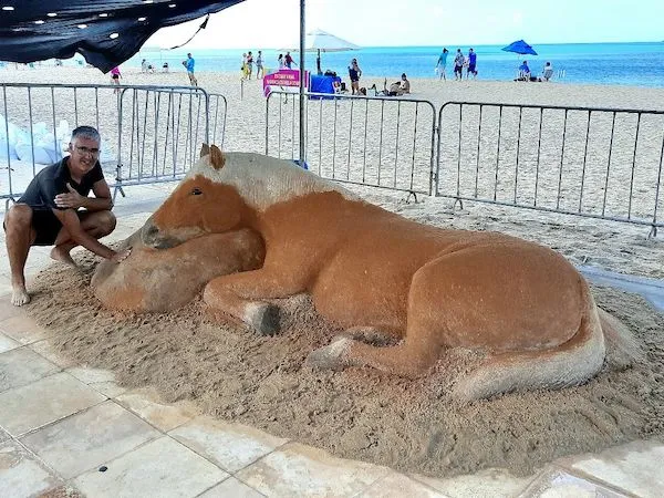 Piesocha kôň na pláži, vytvorený detailne umelcom. More a pláž v pozadí s niekoľkými ľuďmi.