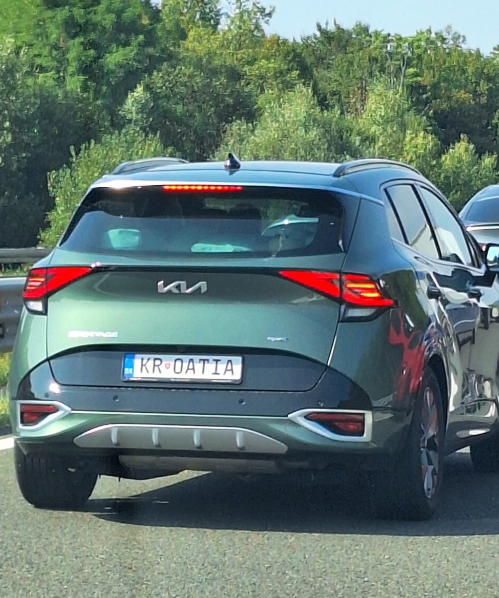 Zelený automobil Kia Sportage so špeciálnou ŠPZ „KROATIA“ na ceste, obklopený zeleňou v pozadí.