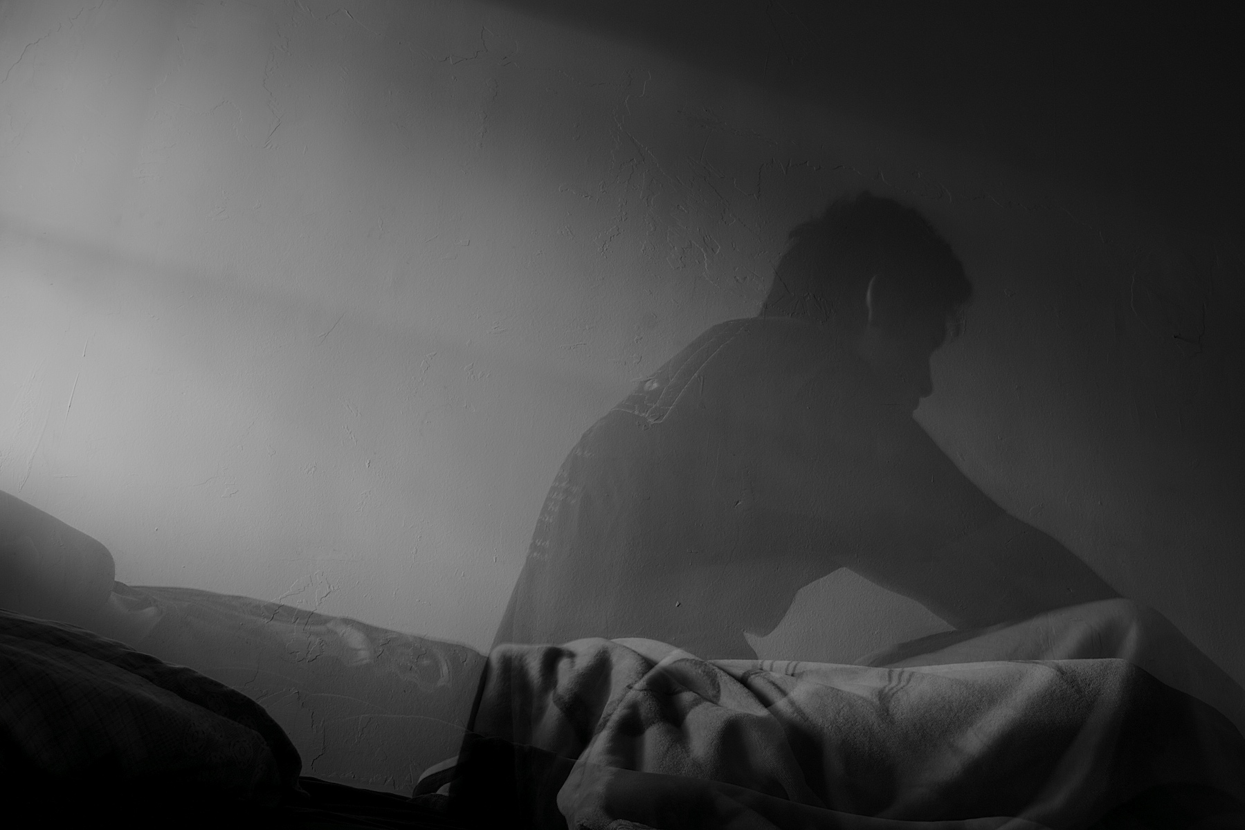 Silueta v tmavej izbe pri slabom osvetlení, zachytená v momentke na posteli.