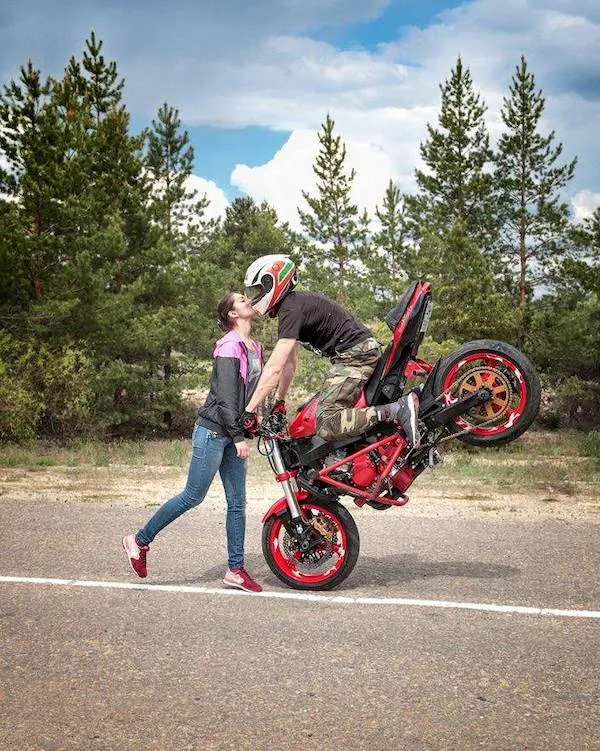 Motorkár na zadnom kolese bozkáva ženu na opustenej ceste, obklopení prírodou.