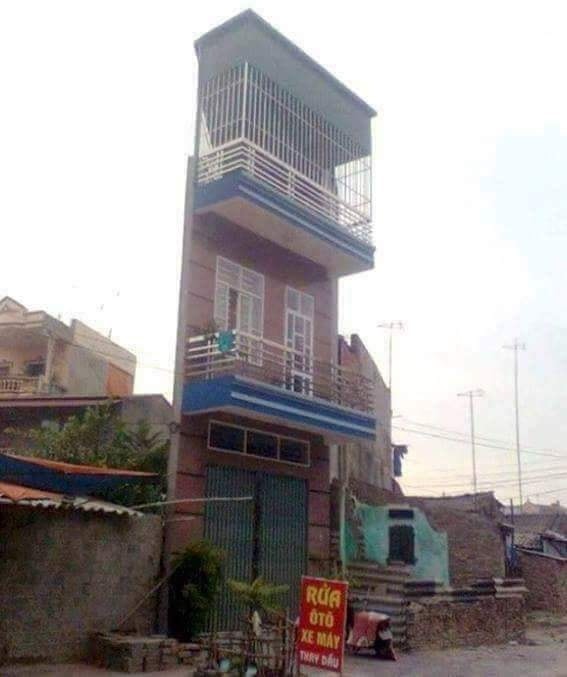 Úzka výšková budova s balkónmi a nápisom na reklamnej tabuli pred vchodom.