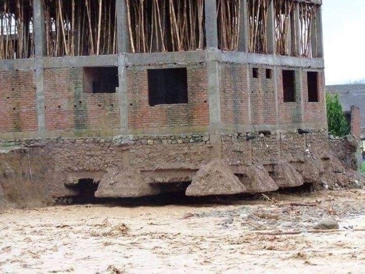 Nedokončená tehlová budova s poškodeným základom po erózii pôdy, vyčnievajúce korene stromov.
