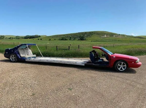 Nezvyčajné predĺžené auto bez strechy a strednej časti zaparkované na vidieckej ceste pri zelenej lúke.