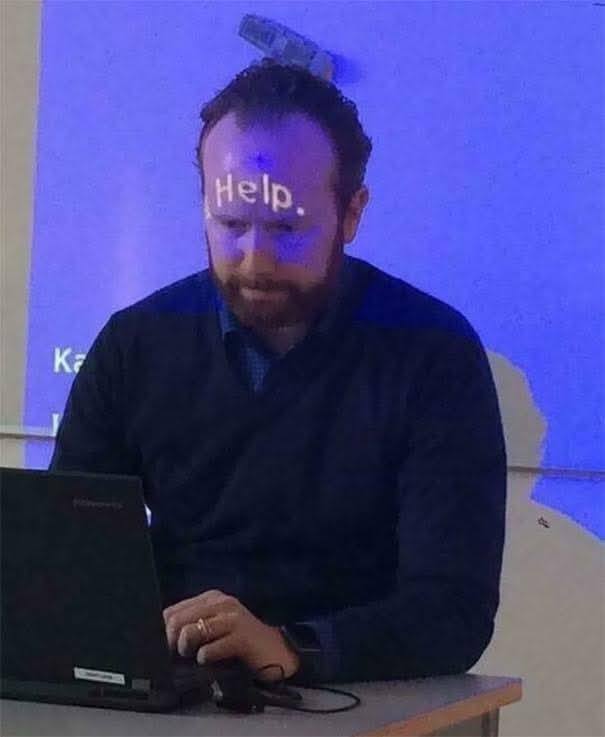 Muž pracuje na notebooku s premietnutým nápisom Help na jeho čele, symbolizujúci potrebu pomoci.