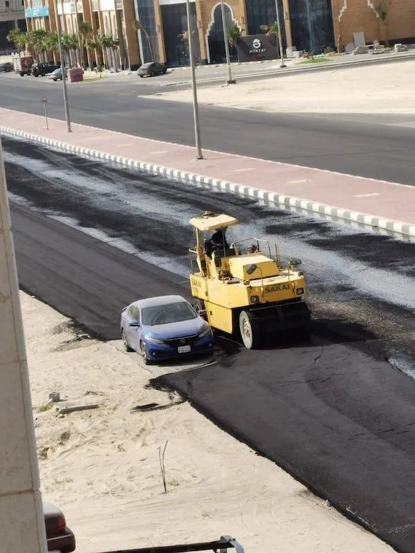 Válec omylom asfaltuje cestu s autom vedľa stavby. Neobyčajná pracovná chyba na rušnej ulici.