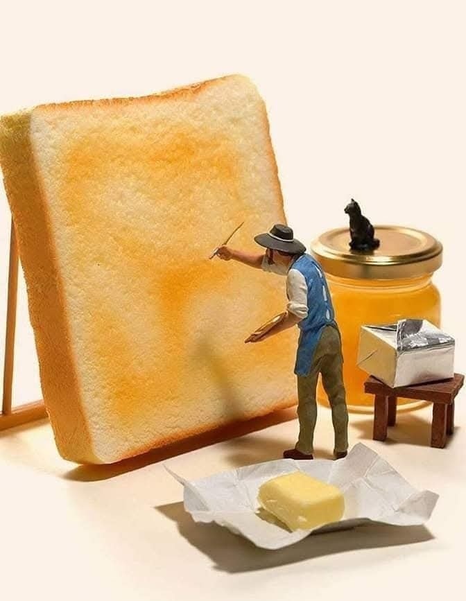 Miniatúrny maliar natiera maslo na toast vedľa medu a masla na stole. Kreatívne jedlo umenie.