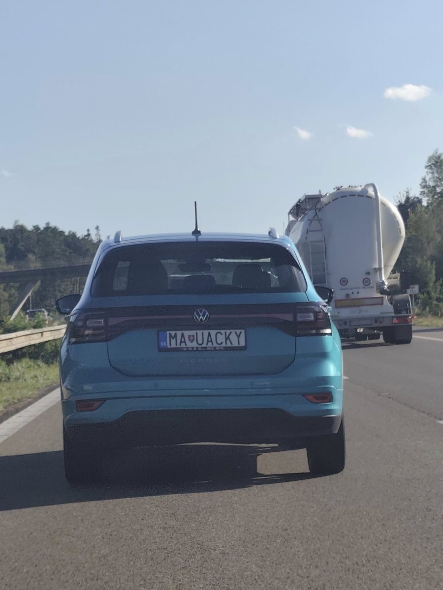 Modré SUV Volkswagen T-Cross s netradičnou poznávacou značkou na diaľnici vedľa bieleho nákladného auta.