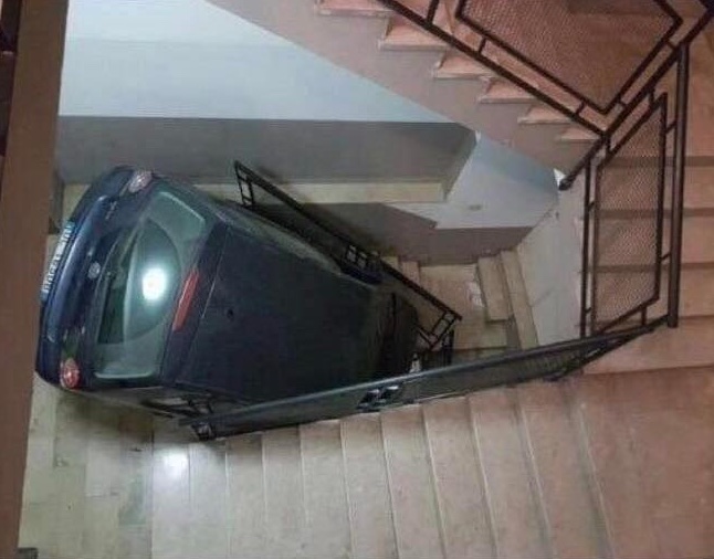 Auto uviaznuté na schodoch vo vnútornom priestore, pohľad zhora, ukazuje netradičnú situáciu pri parkovaní.