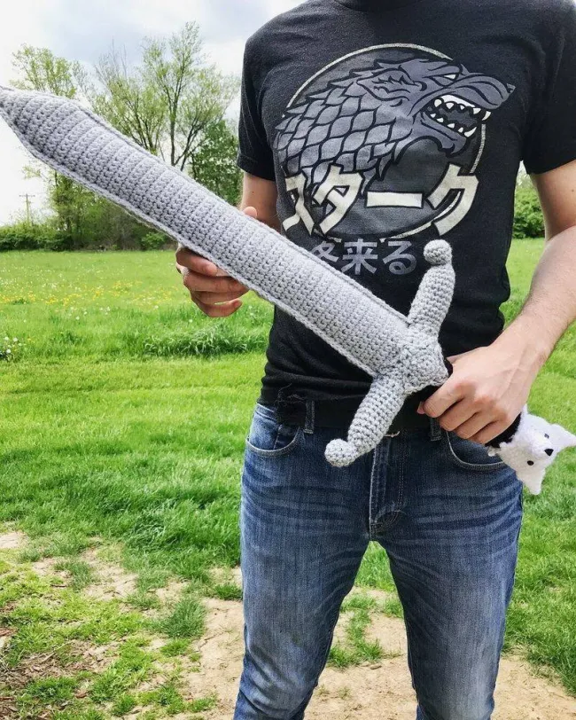 Osoba v tričku s vlkom drží veľký pletený meč v prírode.