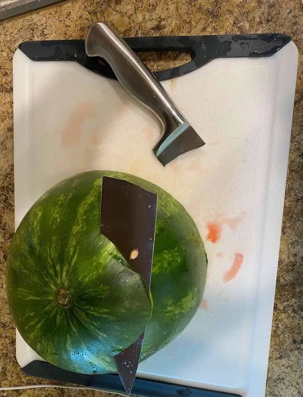 Melón s čepeľou noža uviaznutou vo vnútri, položený na doske na krájanie.