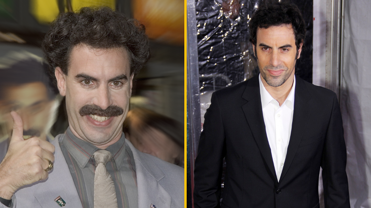 Osoba v šedej bunde s zdvihnutým palcom vedľa muža v saku na červenom koberci.