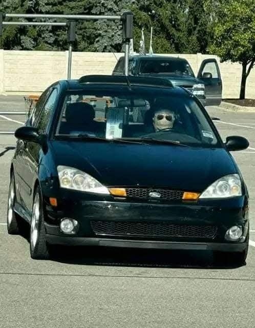 Čierne auto stojí pred semaforom, vodič s okuliarmi sedí za volantom.