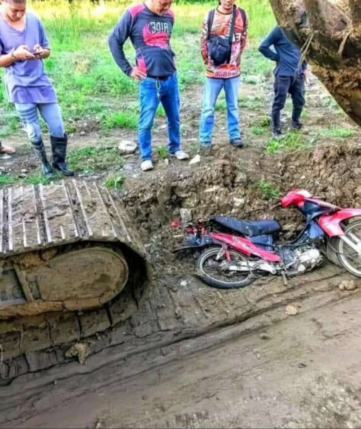Motorka v blate vedľa pásového vozidla, obklopená ľuďmi na stavenisku.
