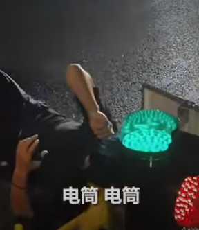 Osoba na zemi vedľa svetelných signálov s čínskym textom, nočná scéna na ceste.