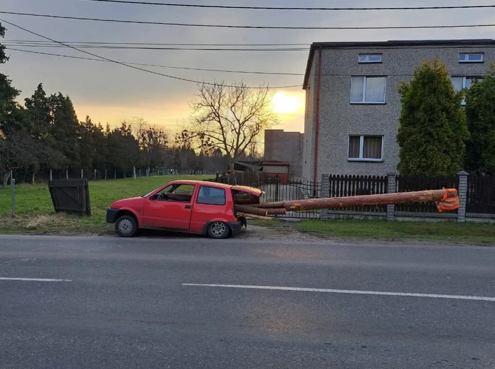 Červené auto s polámaným zadným kolesom uviaznuté na ceste so slnkom klesajúcim za dom.