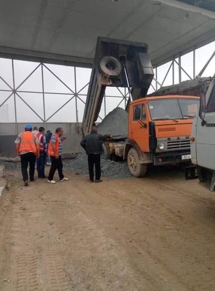 Stavebný kamión vykladá štrk v hale, pracovníci v reflexných vestách sledujú proces.