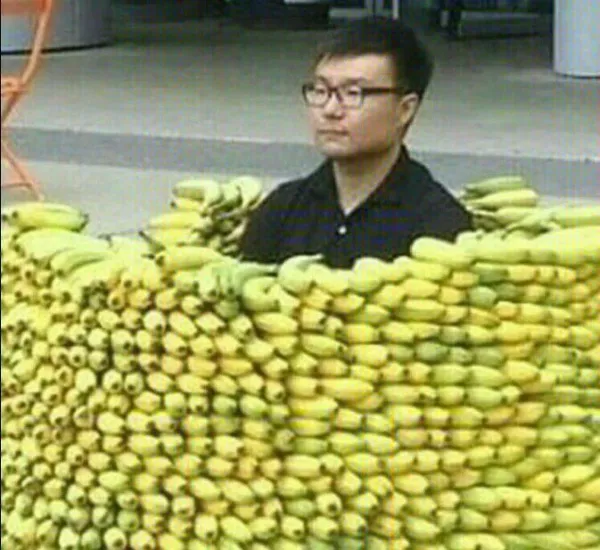 Muž obklopený kôpkou banánov na ulici, sedí medzi hlávkami ovocia v improvizovanom banánovom „hrade“.