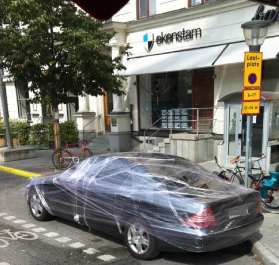 Auto obalené fóliou na ulici pred budovou s bicyklom v pozadí.
