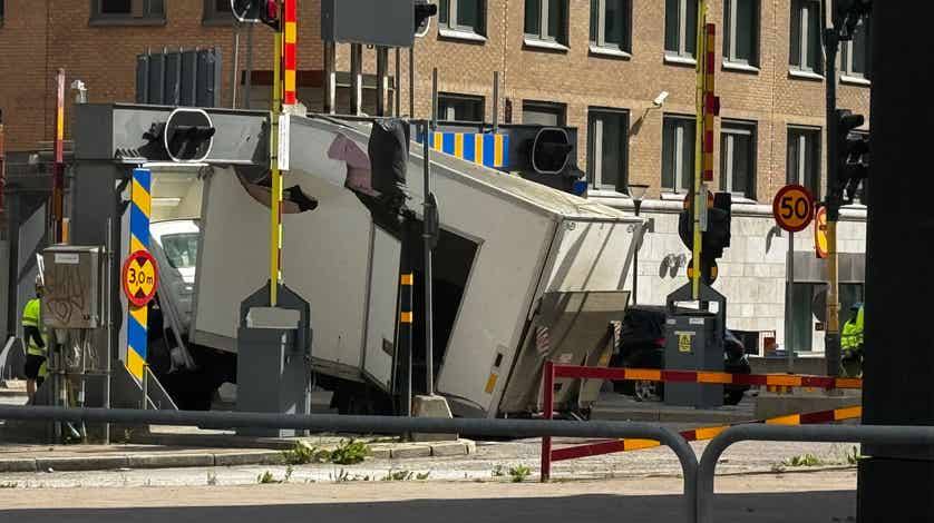 Nákladné auto uviaznuté pod železničným mostom, zobrazené v mestskom prostredí. Dopravné značenie pri moste.