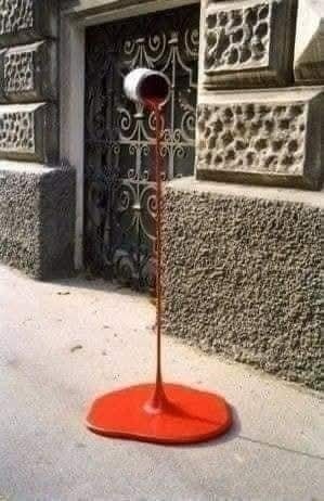 Podivná socha: červená kvapalina s bielym očkom na vrchole pred kamennou budovou.