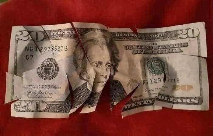 Zničená dvadsaťdolárová bankovka na červenom pozadí, ilustrujúca koncept finančnej degradácie.