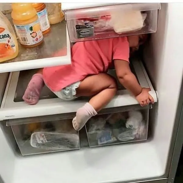 Dieťa lezie do chladničky, skúma vnútro v ružovom oblečení. Vtipná momentka detskej zvedavosti.