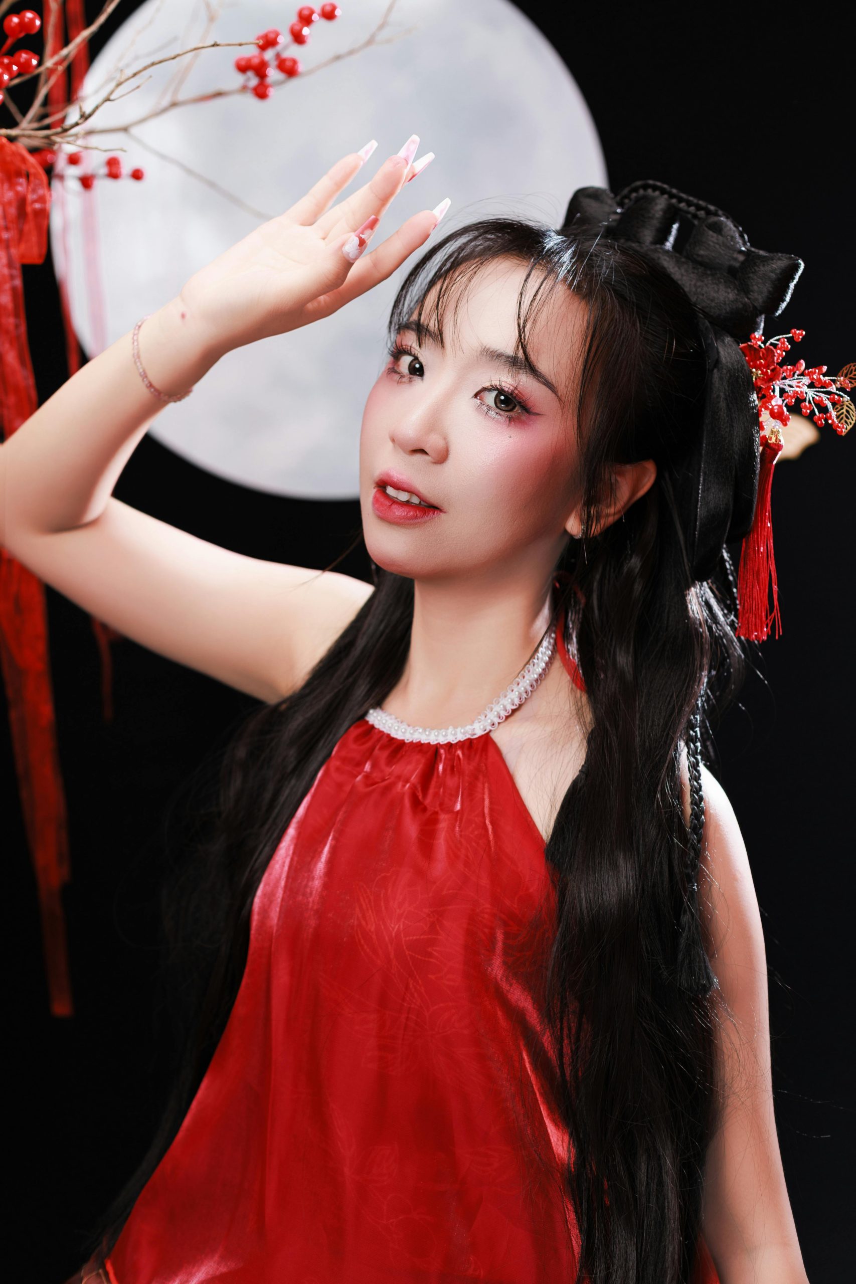 Žena v červenom šate so zdobenými nechtami a vlasmi, na pozadí mesiac a červené dekorácie.